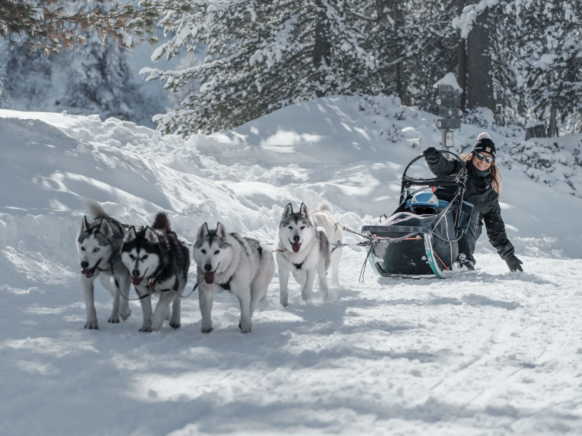 Naturparks Fanes-Sennes-Prags und Puez-Geisler | Chalet Löm Eine Frau fährt mit einem Hundeschlitten durch eine verschneite Landschaft