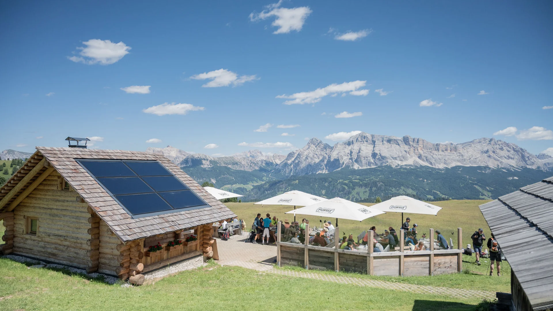 Almhütte mit Solarpaneelen und sonniger Terrasse vor einer Bergkulisse