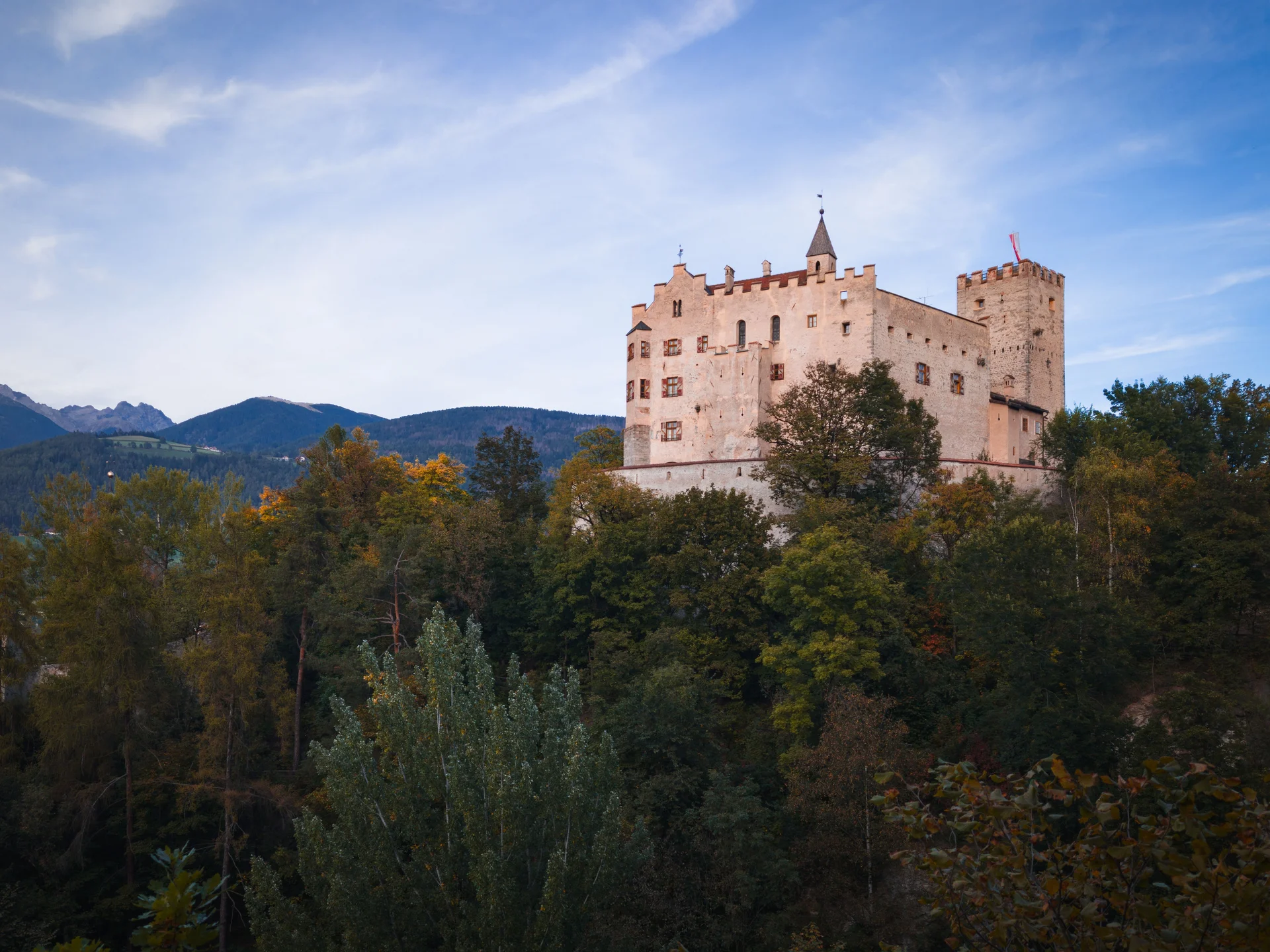 Historische Burg über einem bewaldeten Hang vor einer Bergkulisse