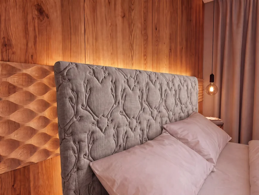 Bett mit gepolstertem Kopfteil vor einer warm beleuchteten Holzwand