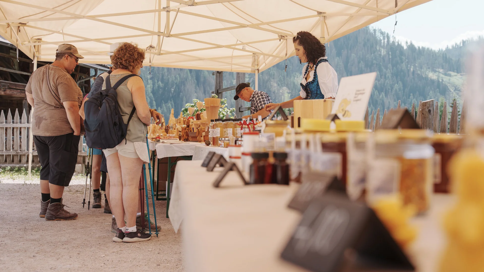 Besucher stöbern an einem Marktstand unter einem Sonnendach vor Bergkulisse