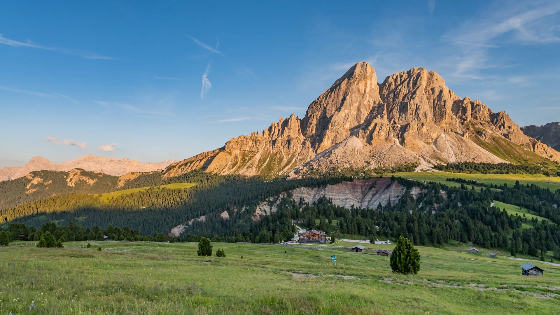Sonnige Almwiese vor bewaldeten Hängen und schroffen Dolomitengipfeln
