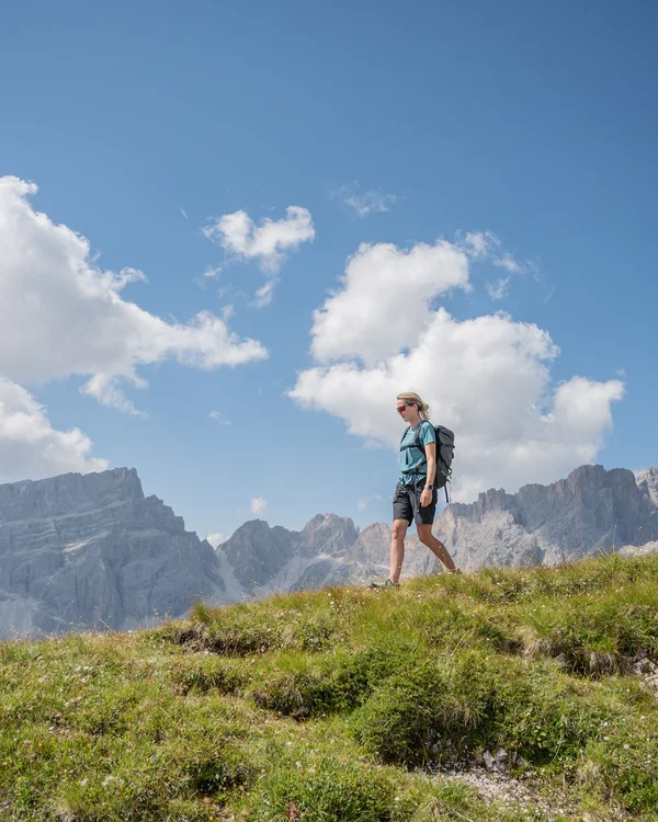 Wanderin mit Rucksack auf einem Bergpfad vor einer felsigen Bergkulisse