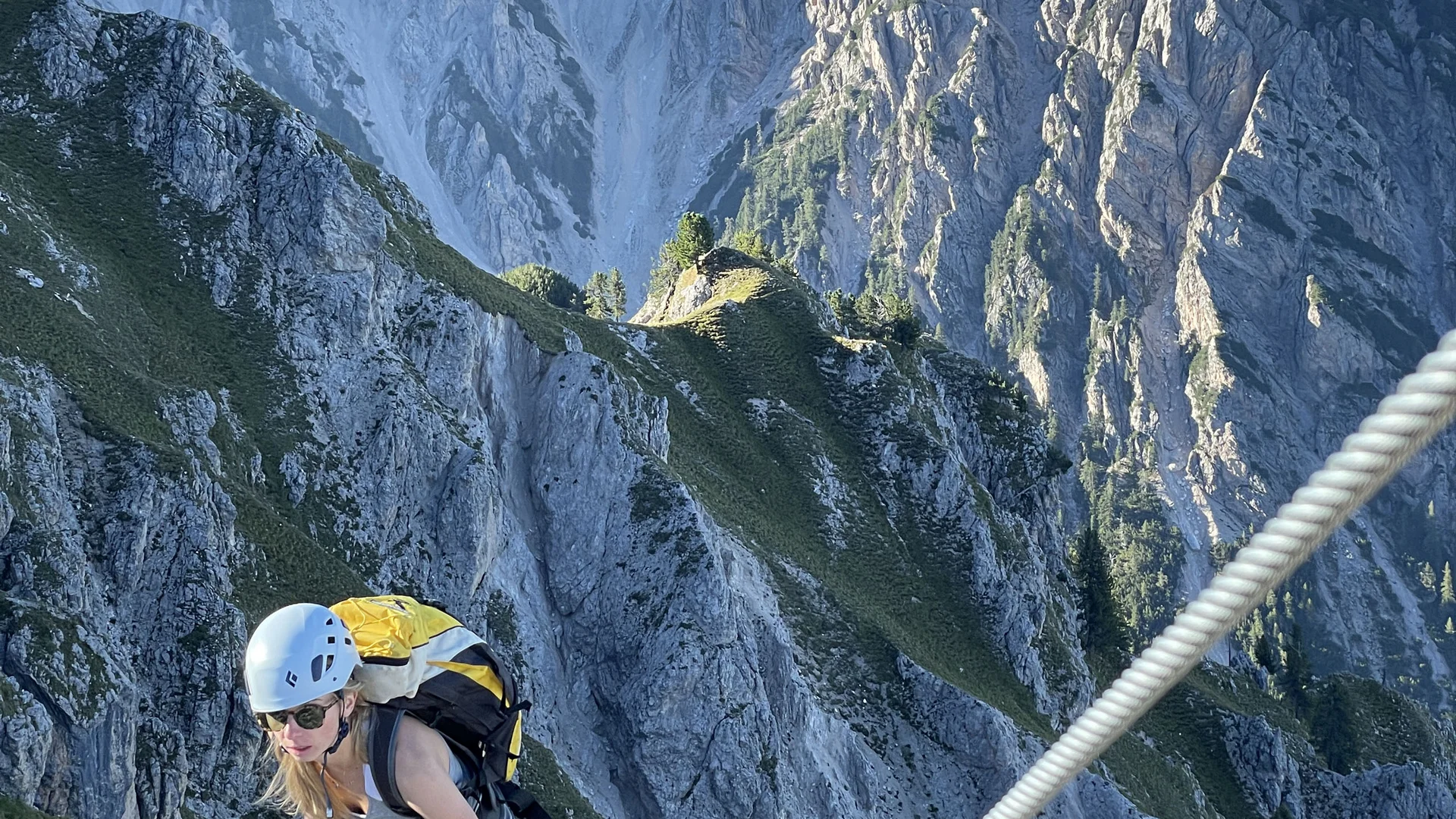 Zwei Bergsteiger mit Helmen klettern an einem Seil über einen steilen Felsgrat