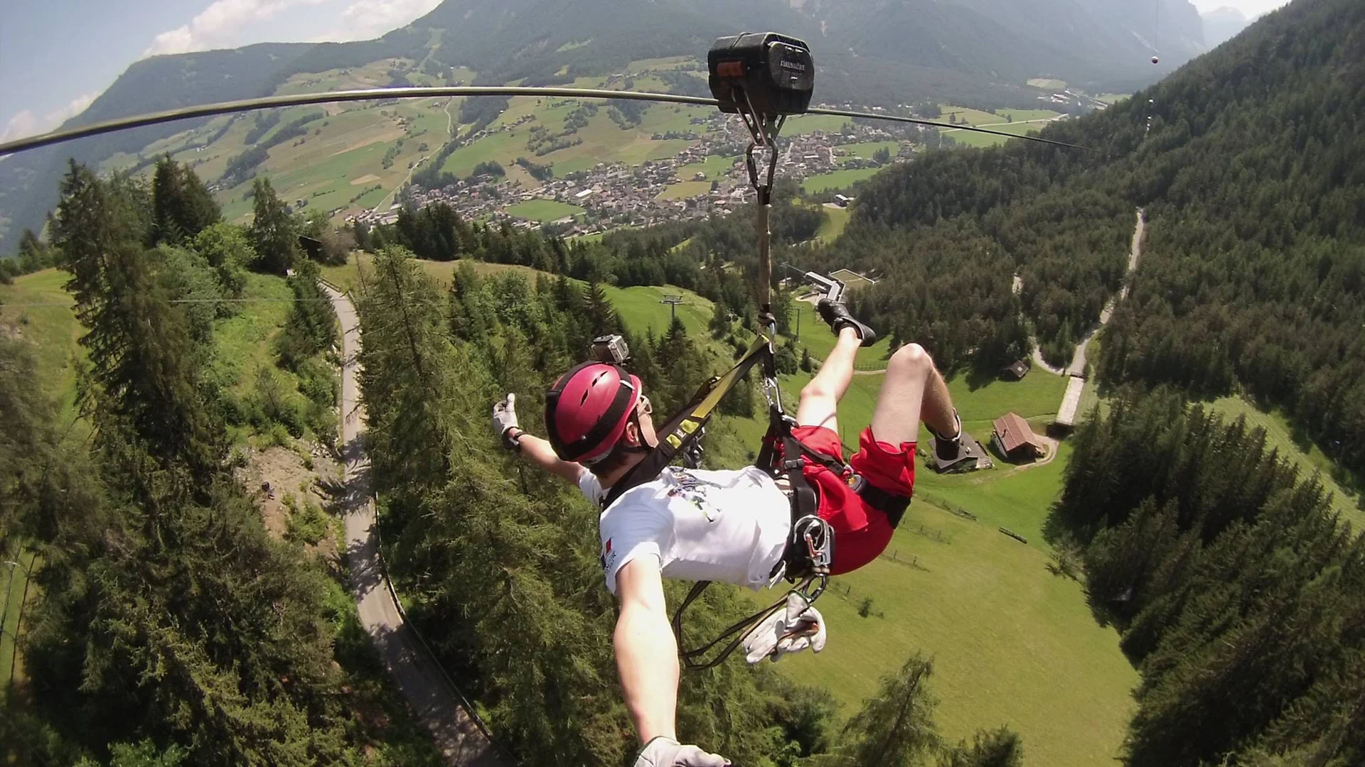 Person fährt an einer Seilrutsche über ein bewaldetes Tal mit Bergkulisse