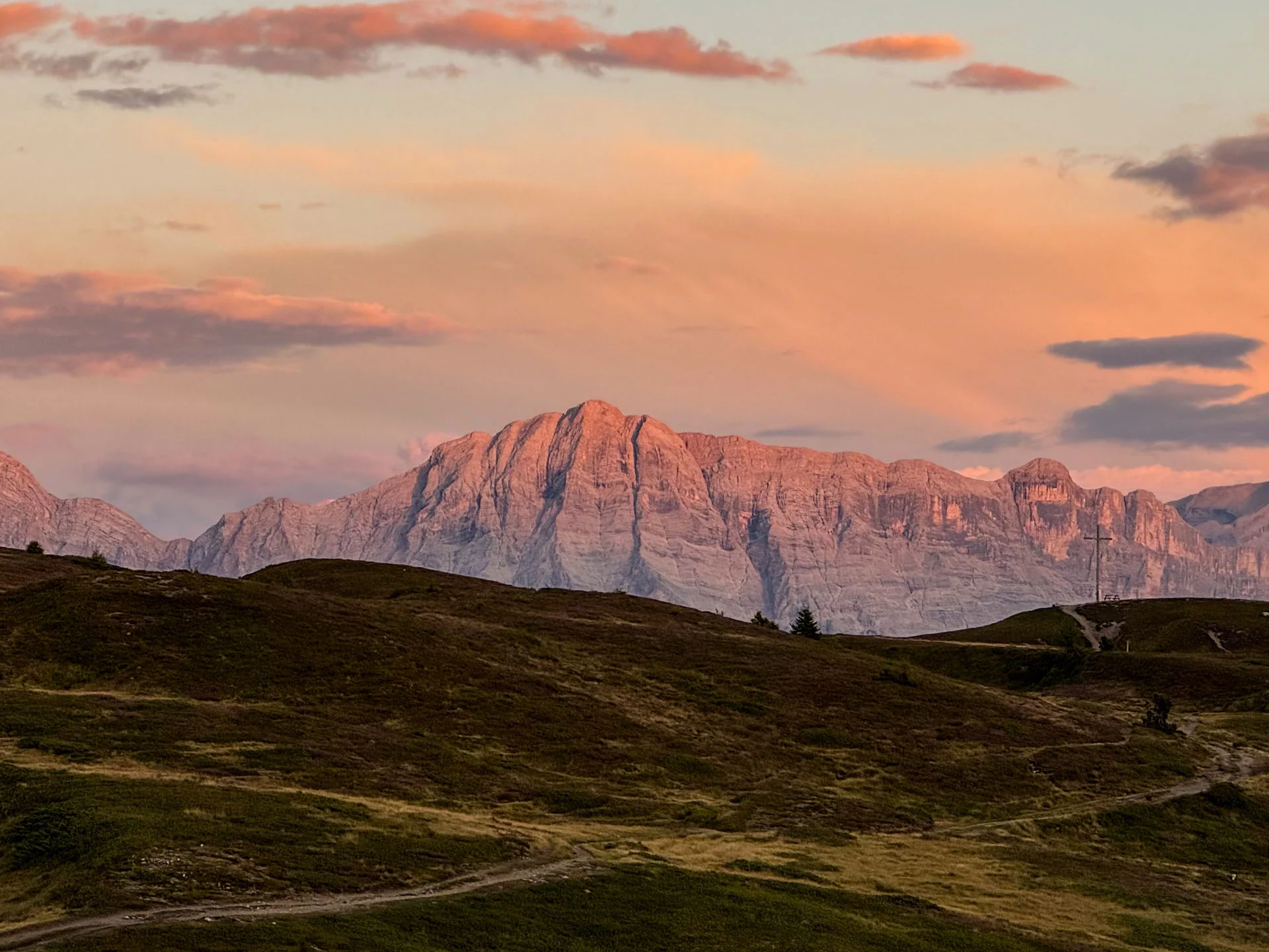 Alpengipfel leuchten im Abendlicht über dunklen, sanft hügeligen Wiesen
