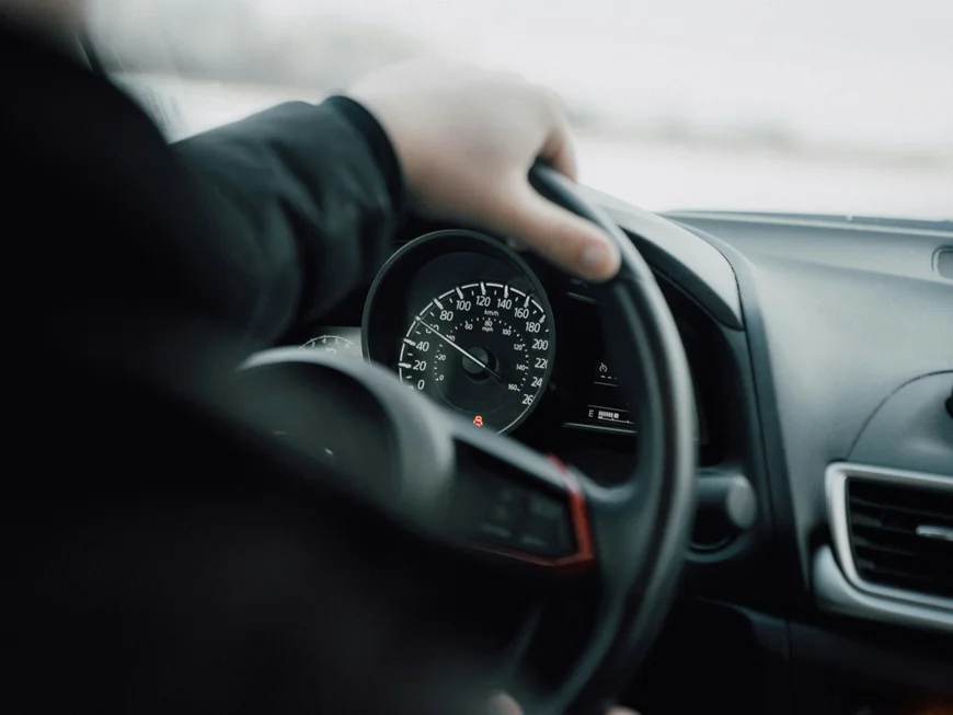 Hand am Lenkrad eines Autos, dahinter Tacho und Armaturenbrett