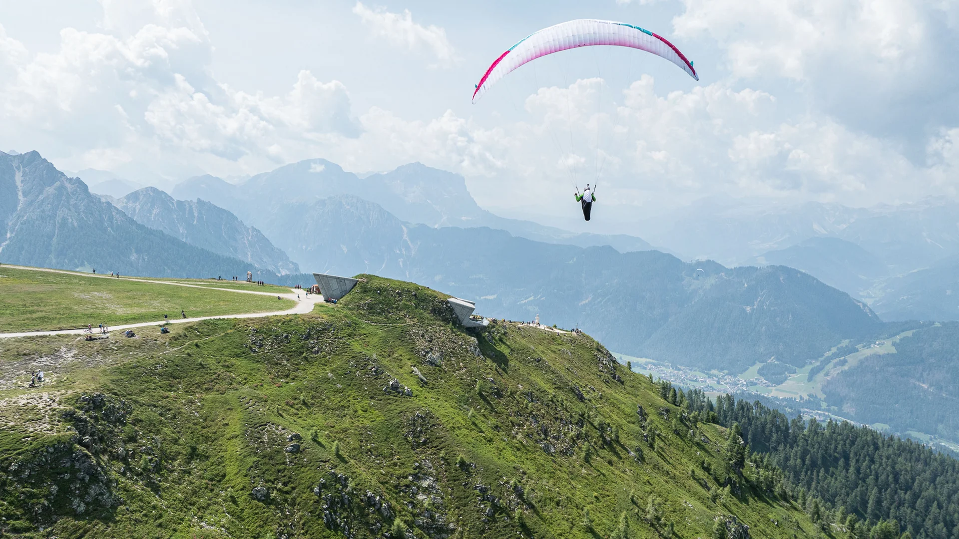 Gleitschirmflieger über einem grünen Bergrücken vor einer Bergkulisse