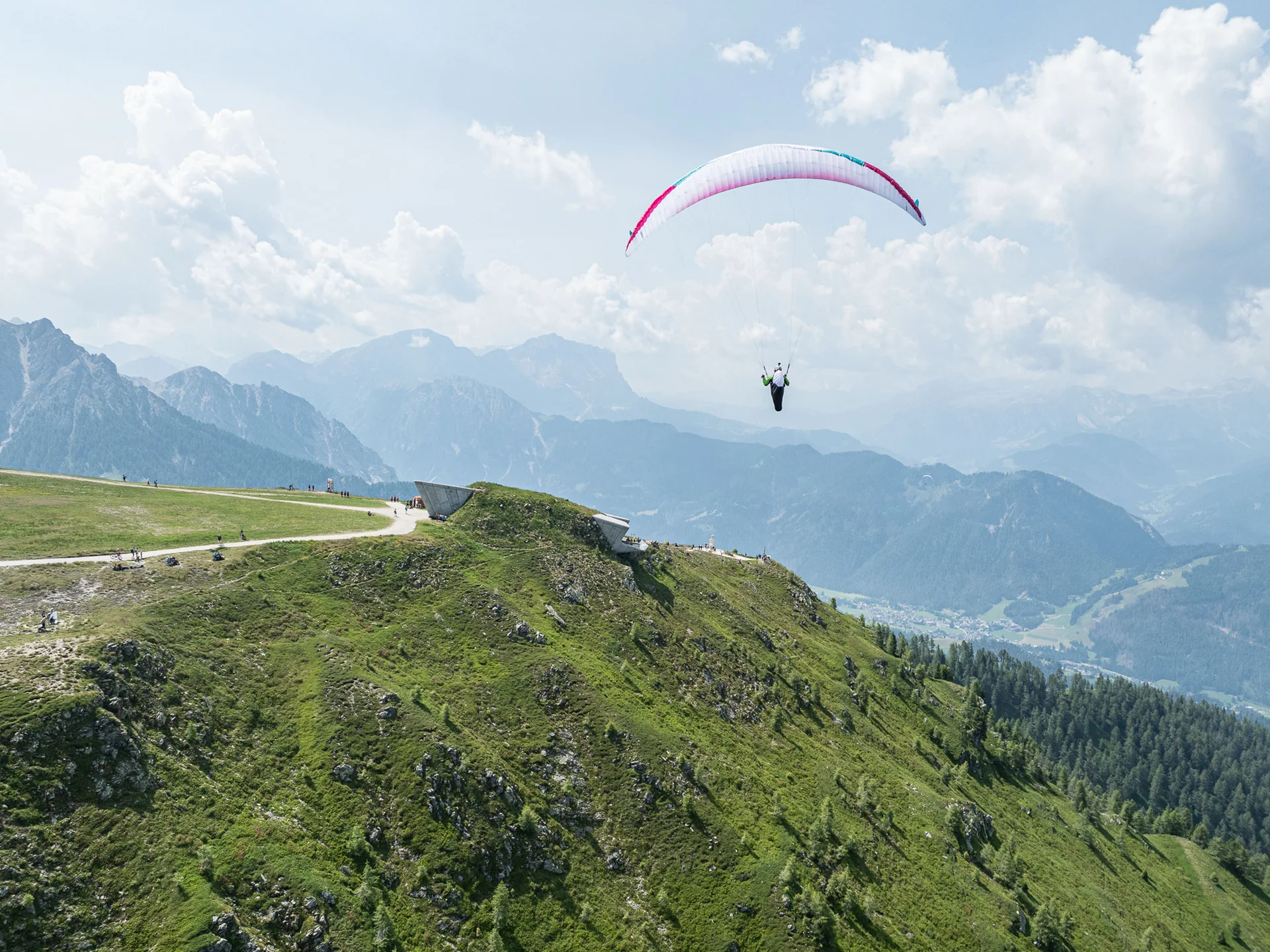Naturparks Fanes-Sennes-Prags und Puez-Geisler | Chalet Löm Gleitschirmflieger über einem grünen Bergrücken vor einer Bergkulisse