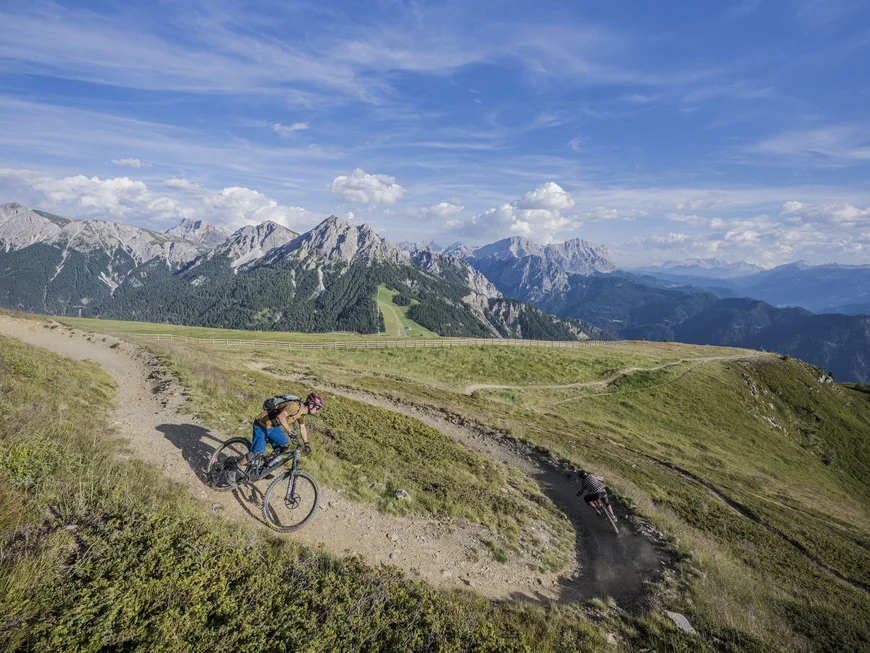 Naturparks Fanes-Sennes-Prags und Puez-Geisler | Chalet Löm Mountainbiker fahren auf einem Bergpfad vor der Kulisse der Alpen
