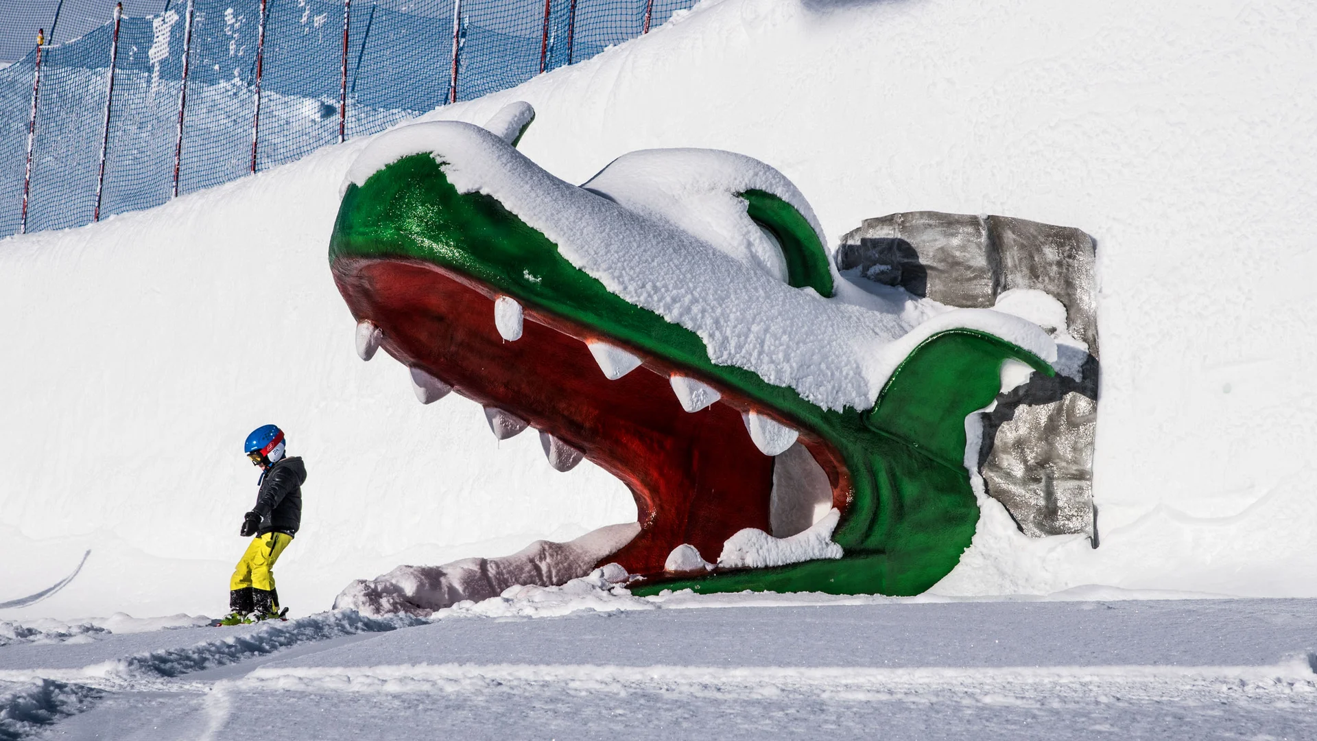 Skifahrer neben einem großen, schneebedeckten Krokodilmaul auf der Piste