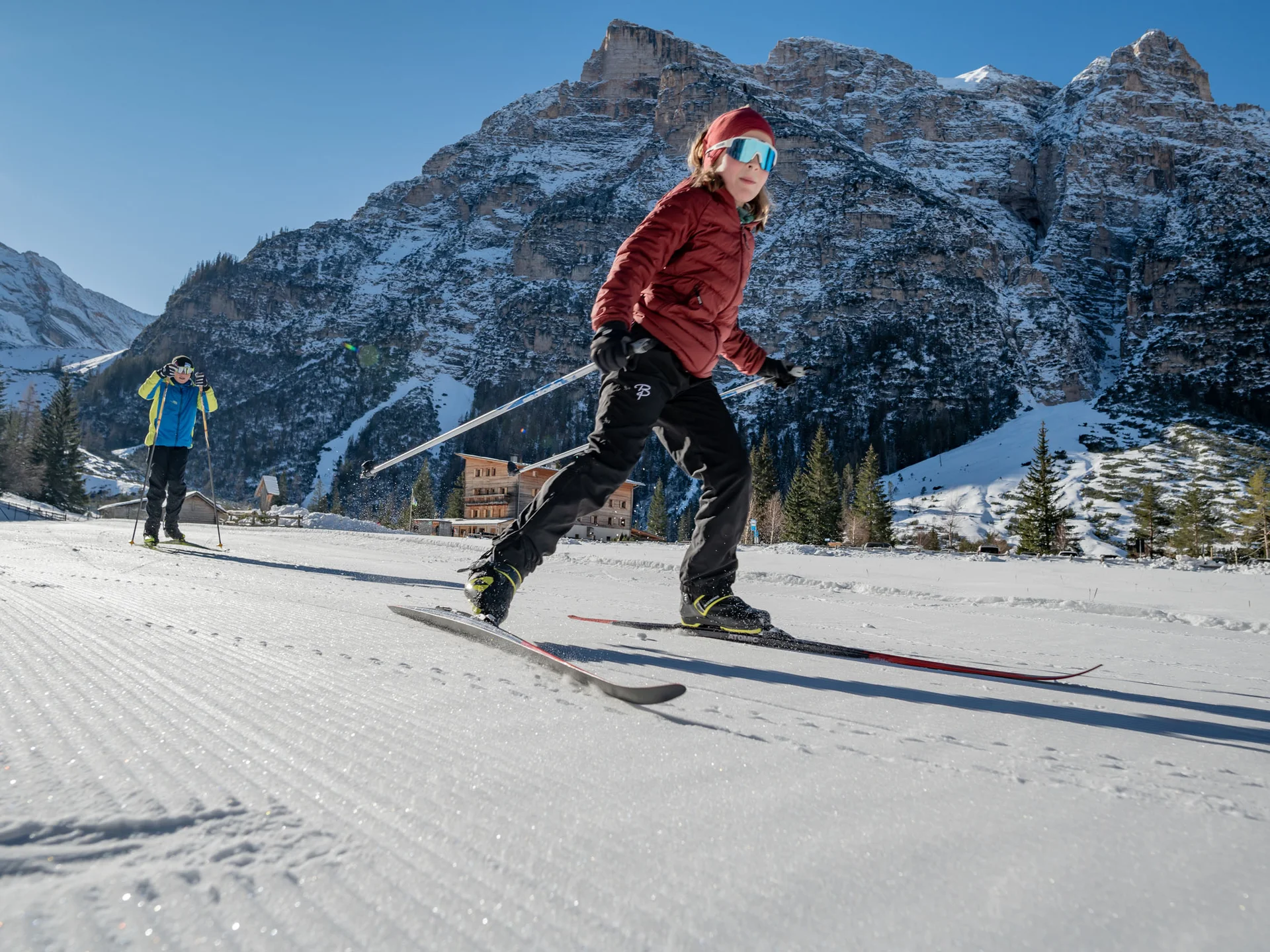 Naturparks Fanes-Sennes-Prags und Puez-Geisler | Chalet Löm Skifahrerin auf einer Loipe vor verschneiten Bergen, eine weitere Person im Hintergrund