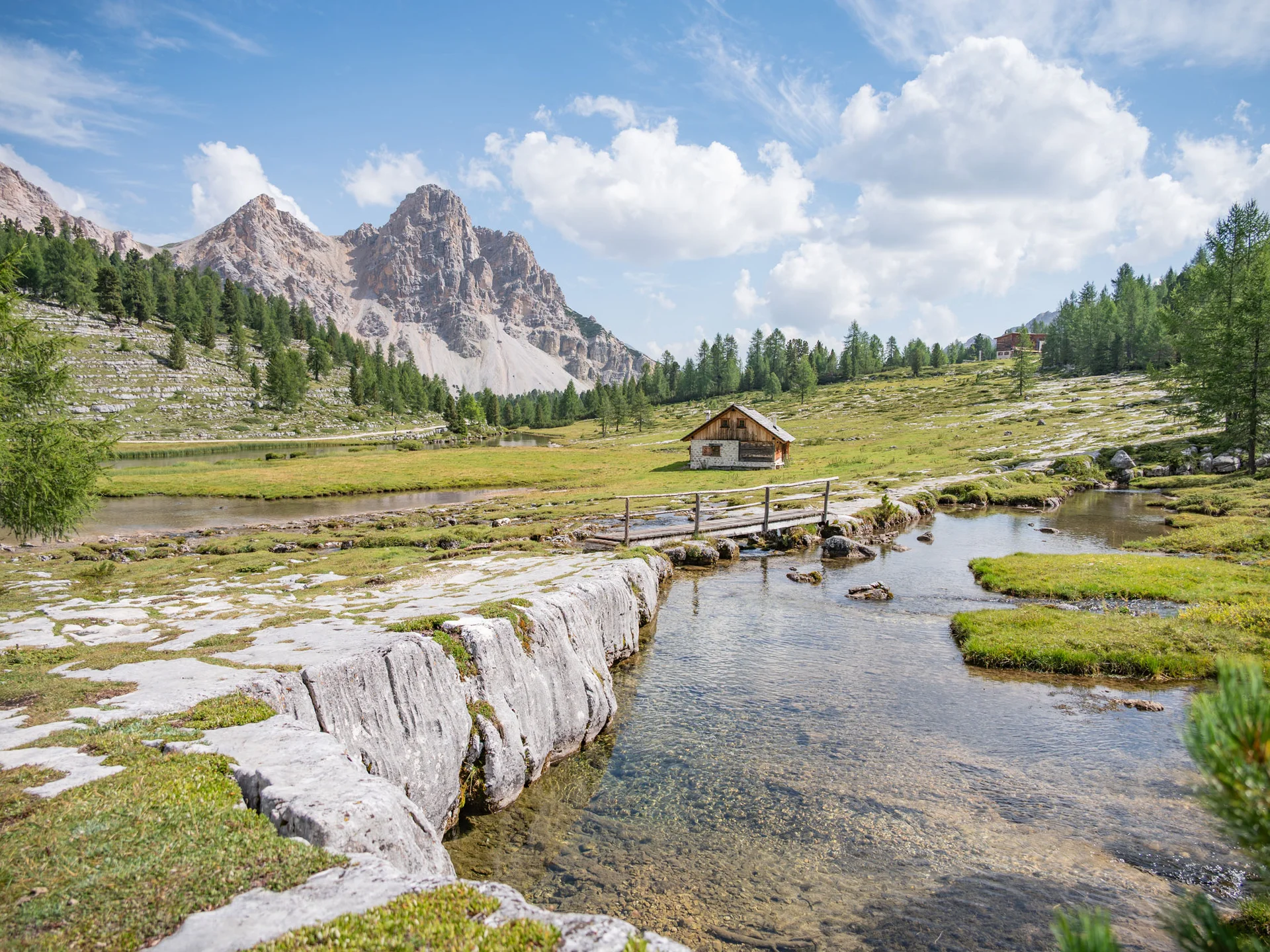 Alpine Berglandschaft mit Bach, Holzbrücke und Hütte vor schroffen Gipfeln