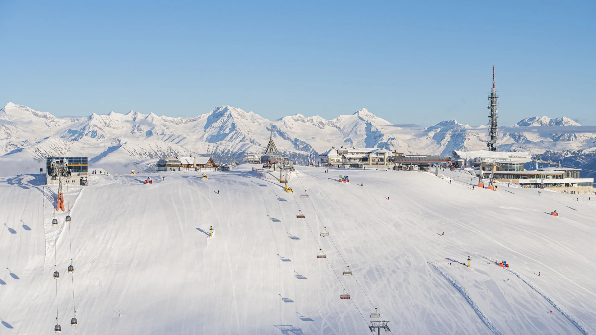 Verschneite Skipiste mit Skiliften und Bergstation vor einer schneebedeckten Alpenkulisse