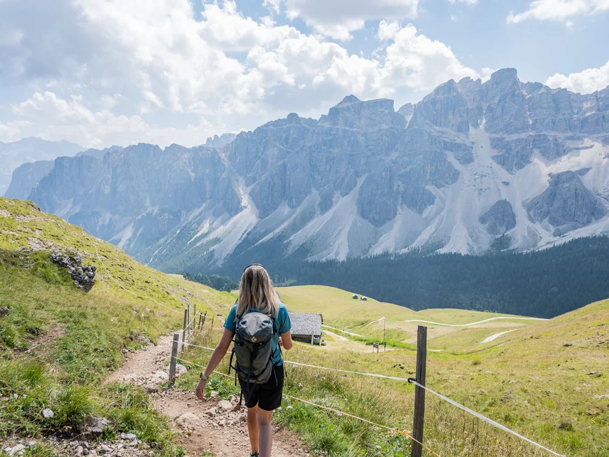 Naturparks Fanes-Sennes-Prags und Puez-Geisler | Chalet Löm Wanderin auf einem Bergpfad mit Blick auf eine imposante Bergkette