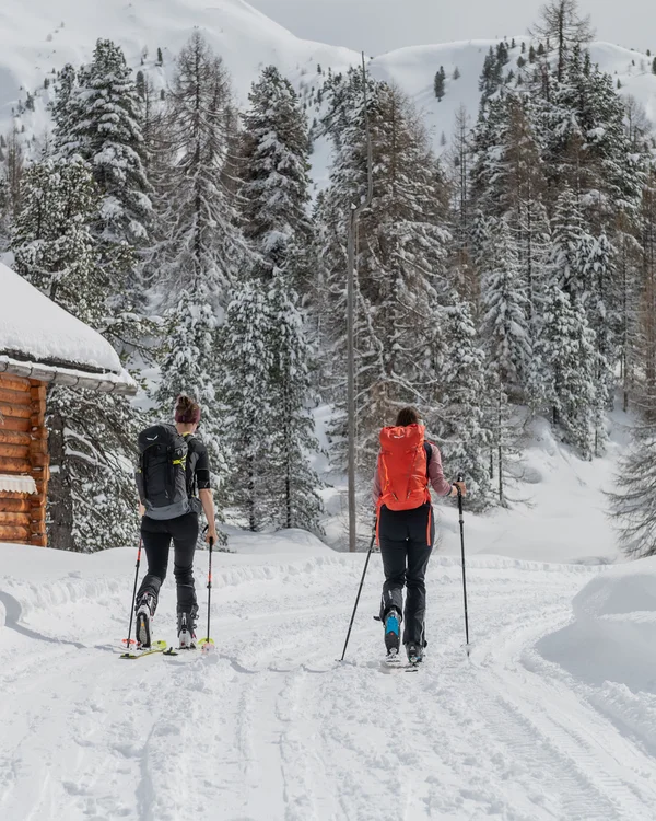 Naturparks Fanes-Sennes-Prags und Puez-Geisler | Chalet Löm Zwei Skifahrer mit Stöcken auf einem verschneiten Weg neben einer Berghütte