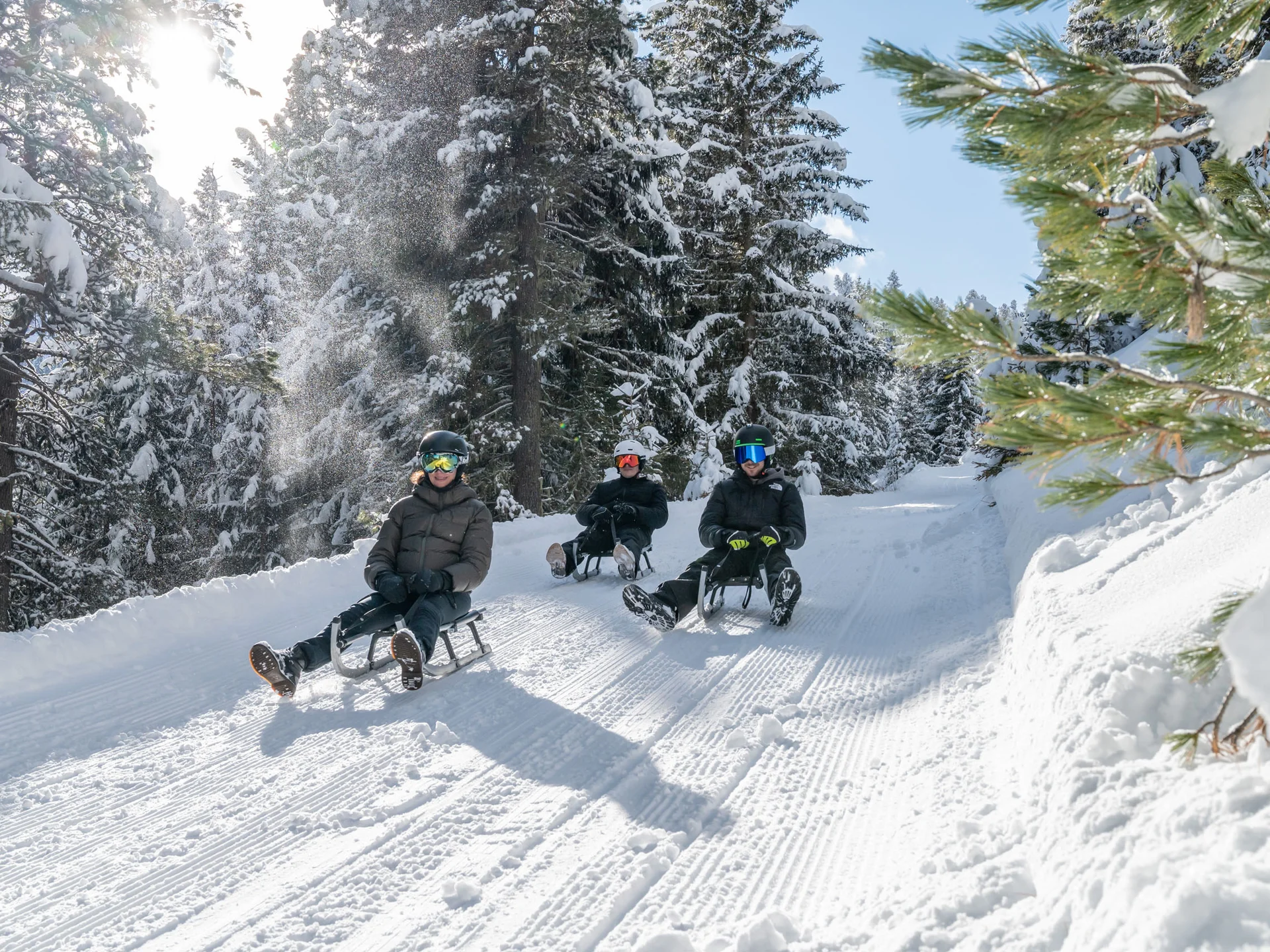 Naturparks Fanes-Sennes-Prags und Puez-Geisler | Chalet Löm Drei Personen rodeln auf einer präparierten Schneepiste durch einen verschneiten Wald