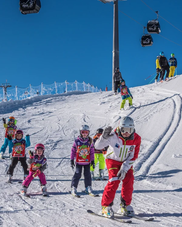 Naturparks Fanes-Sennes-Prags und Puez-Geisler | Chalet Löm Skifahrer und Kinder fahren gemeinsam eine verschneite Piste hinunter, Gondeln schweben darüber