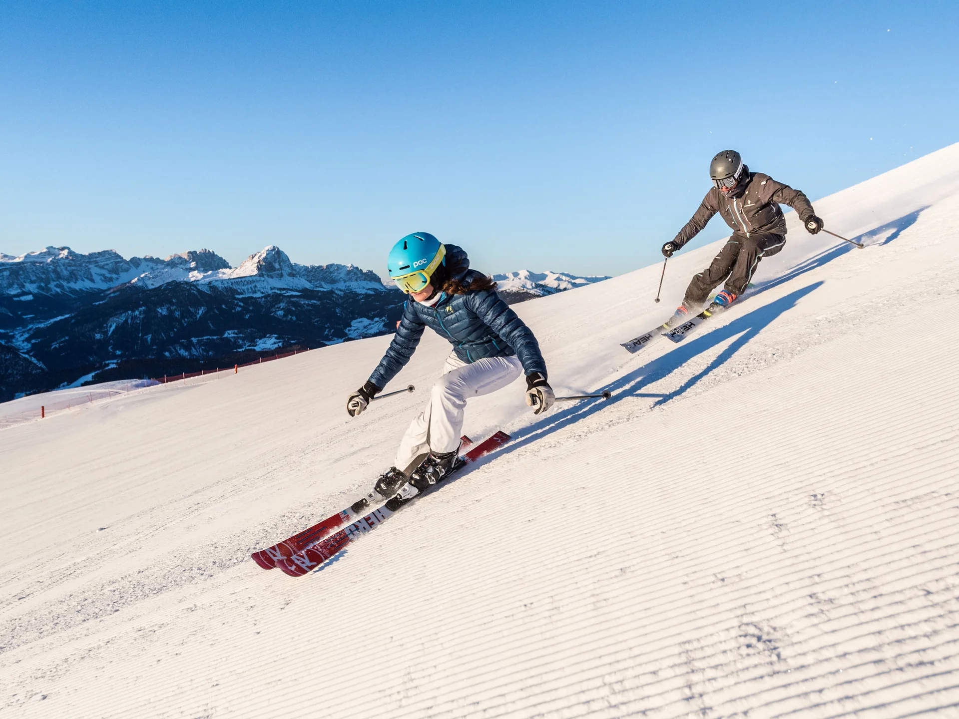 Naturparks Fanes-Sennes-Prags und Puez-Geisler | Chalet Löm Zwei Skifahrer fahren auf einer präparierten Piste vor schneebedeckten Bergen