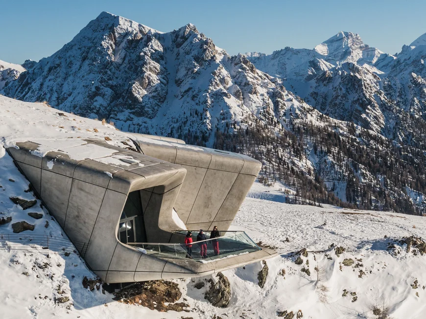 Naturparks Fanes-Sennes-Prags und Puez-Geisler | Chalet Löm Modernes Gebäude mit Aussichtsplattform in verschneiter Berglandschaft, drei Menschen am Geländer