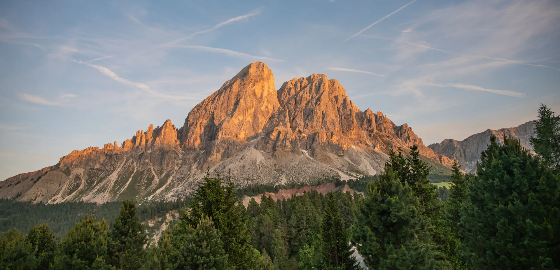 Ihr Chalet in den Dolomiten mit privater Sauna Abendsonne beleuchtet einen zerklüfteten Berg über einem dichten Nadelwald