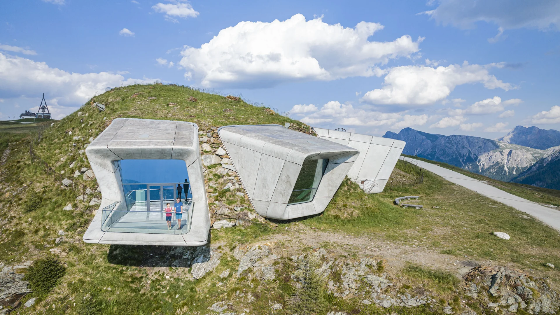 Moderne Betonpavillons am Berghang mit zwei Personen und Bergpanorama